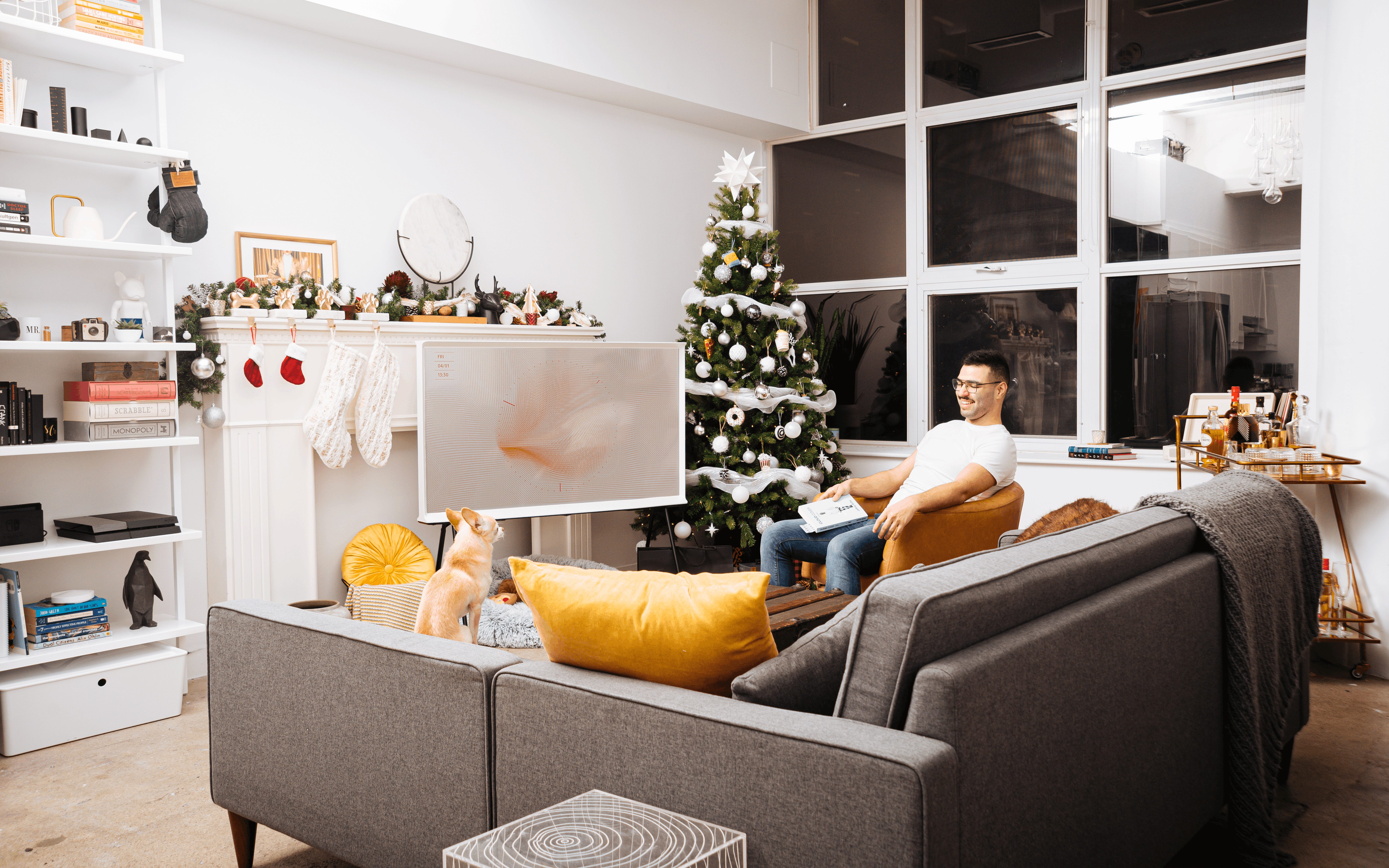 Mann, Der Weißes T Shirt Mit Rundhalsausschnitt Und Brille Hält Buch Hält, Während Auf Stuhl Nahe Weihnachtsbaum Im Wohnzimmer Sitzend
